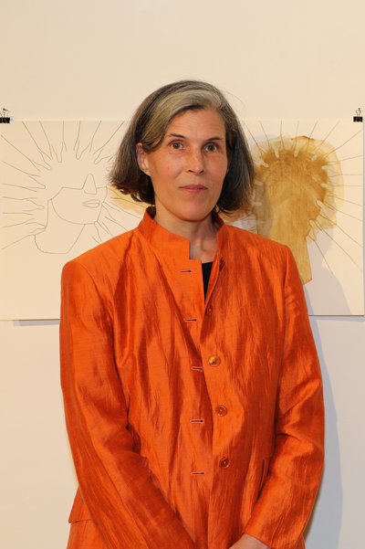 Frau in orangefarbener Jacke vor zwei grafischen Kunstwerken an der Wand.