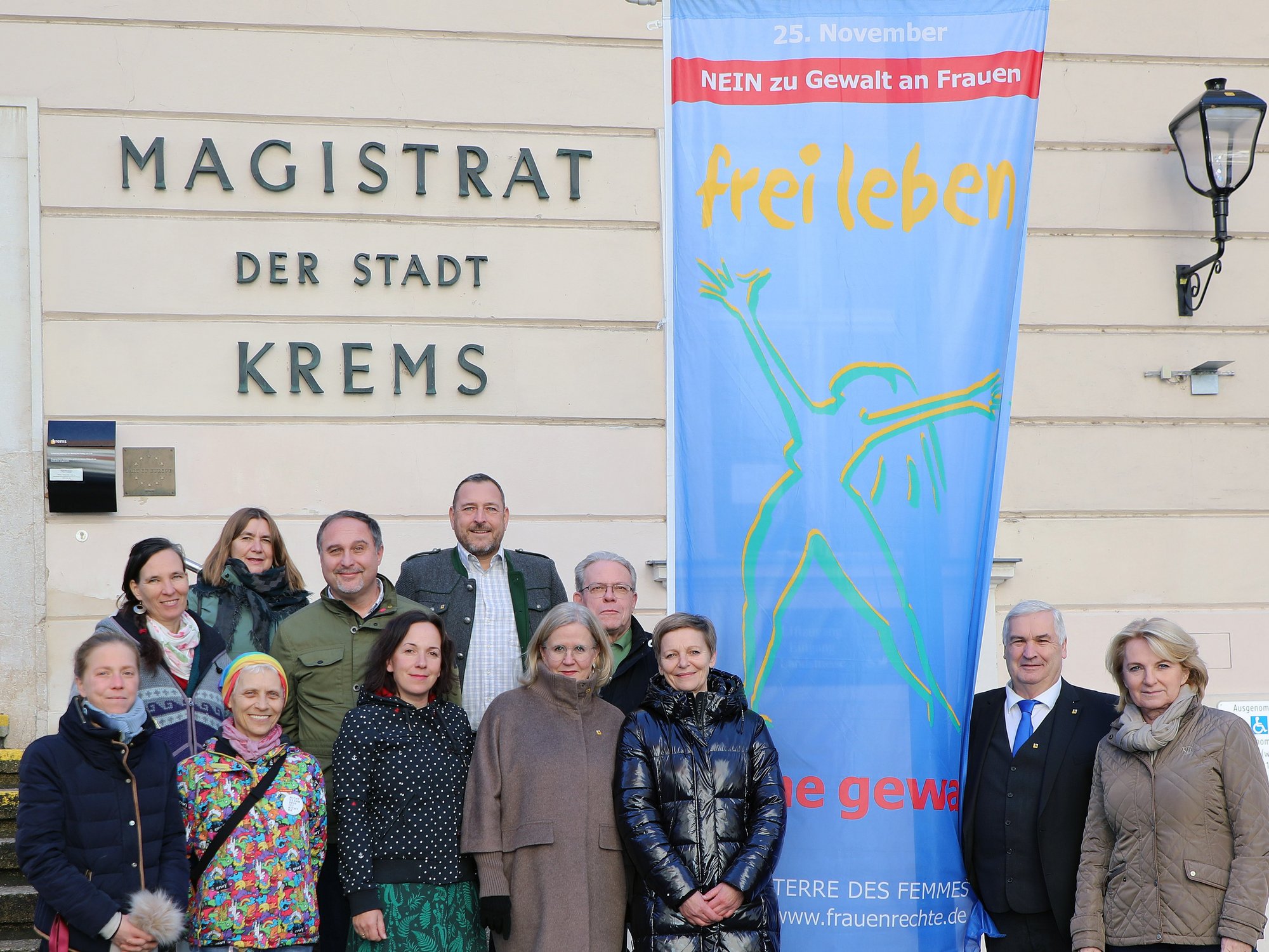 Vertreter aus Stadtpolitik und Frauenberatung vor einer der beiden Fahnen am Kremser Rathaus. 