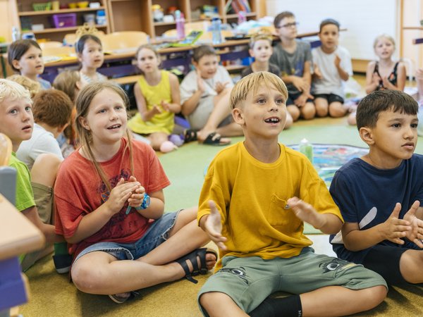 Kinder sitzen in einem Klassenzimmer am Boden und klatschen.