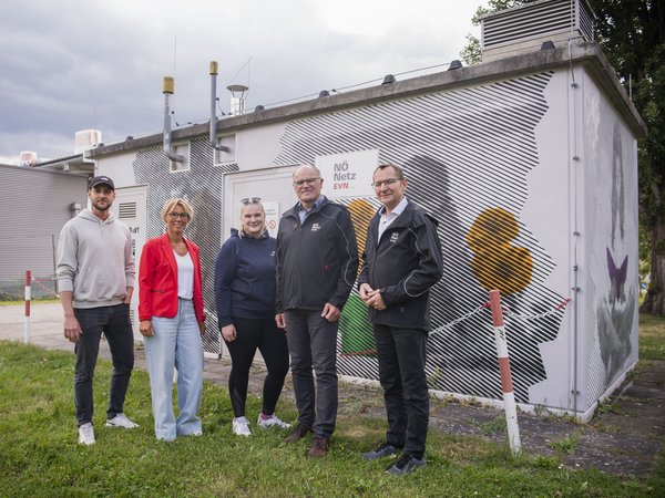 Fünf Personen stehen vor einem von Graffiti verzierten EVN-Gebäude mit der Aufschrift „NÖ Netz“.