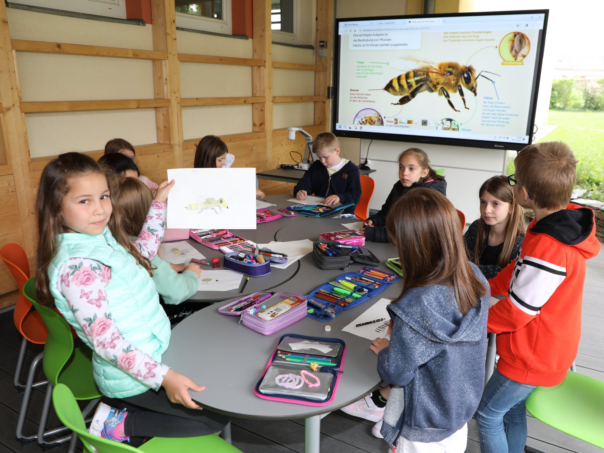 Gruppe Schüler in der Freiluftklasse, ein Mädchen zeigt ein selbstgemaltes Bild einer Biene
