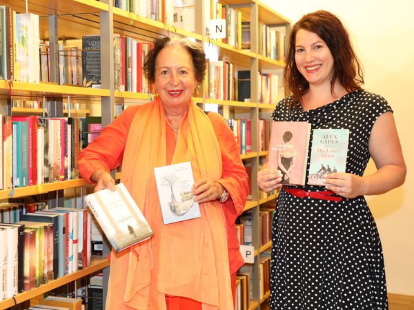 Zwei Frauen mit Büchern in der Hand vor einem Bücherregal in einer Bücherei