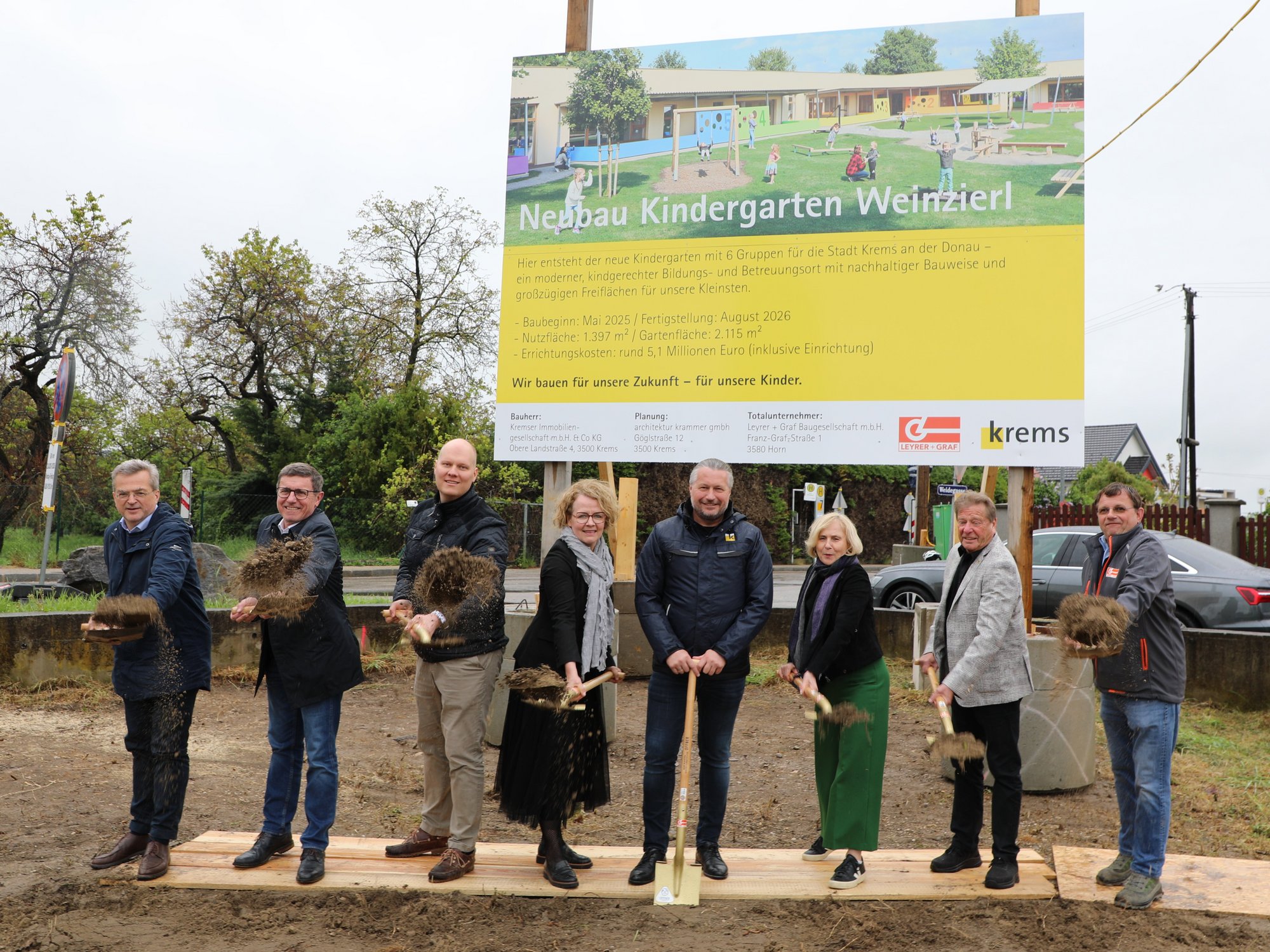 Vertreter aus Politik und Verwaltung mit Spaten vor einer Bautafel mit einem Bild des neuen Kindergartens