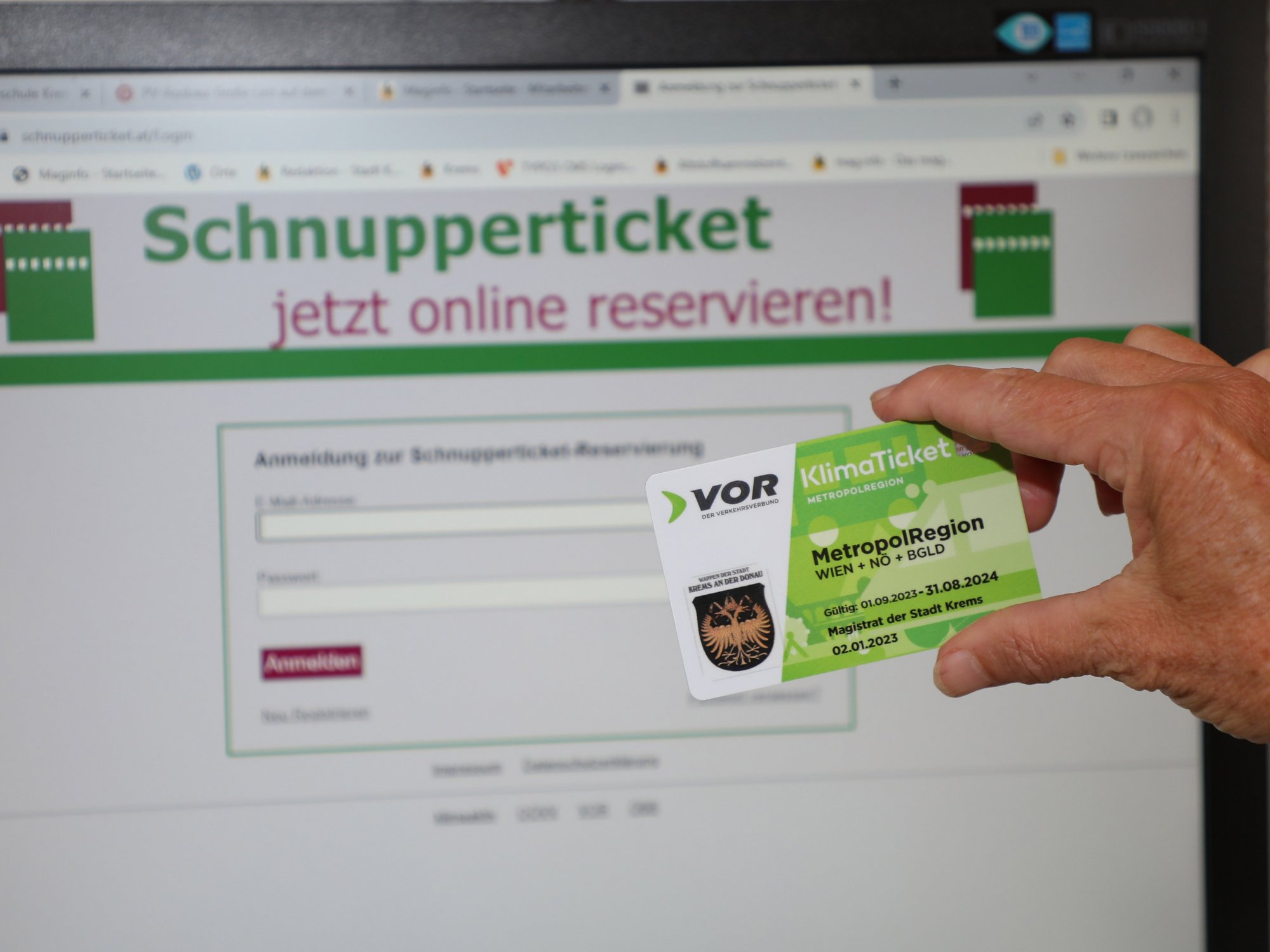 Eine Hand hält eines der Schnuppertickets, im Hintergrund ein PC auf dem die Reservierungsseite geöffnet bist