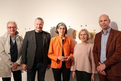 Fünf Personen bei einer Ausstellungseröffnung vor einer Wand mit Porträtzeichnungen.