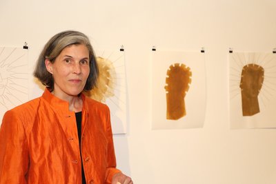Frau in orangefarbener Jacke vor zwei grafischen Kunstwerken an der Wand.