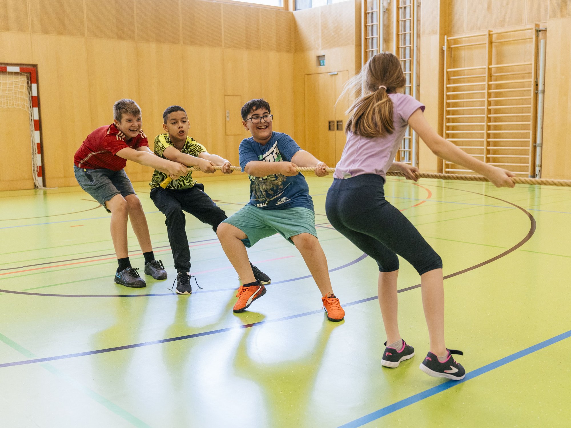 Vier Schüler haben Spaß beim Tauziehen in einer Schulturnhalle