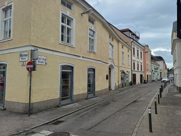 Blick in die Herzogstraße in der Kremser Altstadt mit historischen Gebäuden und Geschäftslokalen bei bewölktem Himmel.