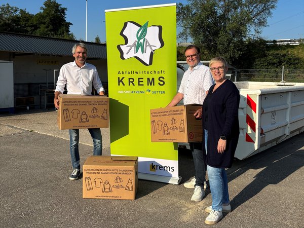 Drei Personen mit Kartons vor einem Banner der Abfallwirtschaft Krems im Sammelzentrum.