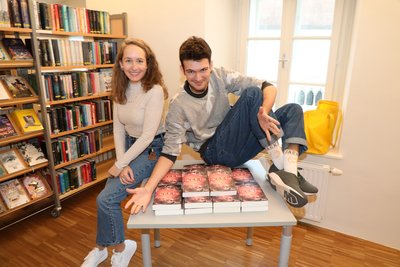 Jugendbuchautor Colin Hadler und die Kremser Büchereileiterin Kathrin Raffetseder, sitzend auf einem Büchertisch