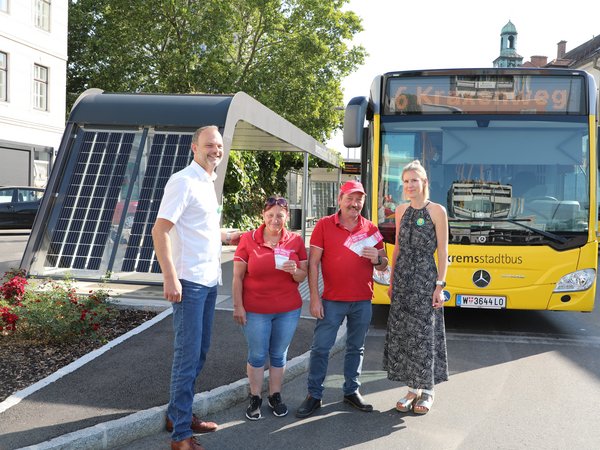 Vier Personen vor einem gelben Stadtbus an einer Bushaltestelle am Kremser Bahnhof