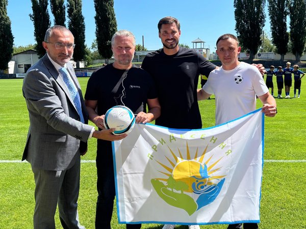 Vier Männer mit Flagge und Fußball auf einem Fußballfeld