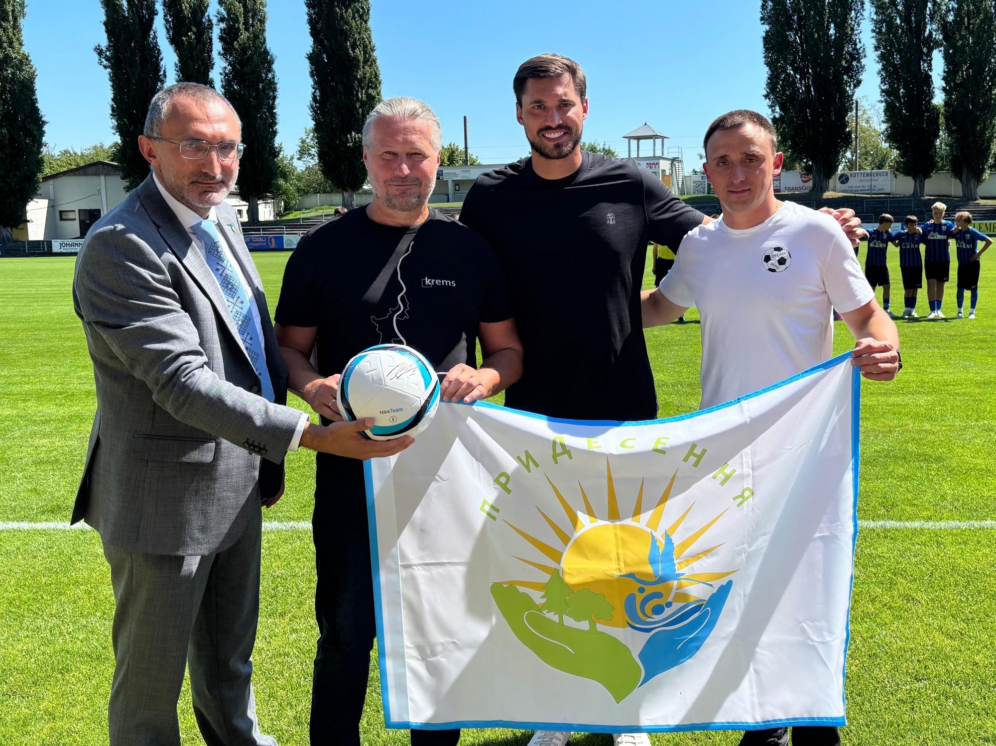Vier Männer mit Flagge und Fußball auf einem Fußballfeld