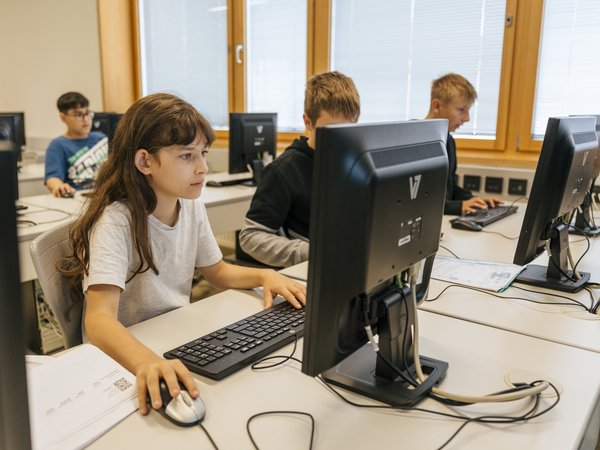 Mehrere Schüler vor PCs im Computerraum einer Schule