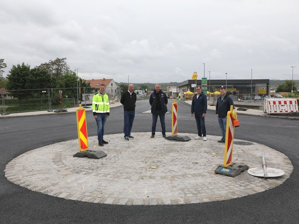 Fünf Männer stehen in der Mitte eines Kreisverkehrs, im Hintergrund sind eine Brücke sowie ein Billa-Supermarkt zu sehen