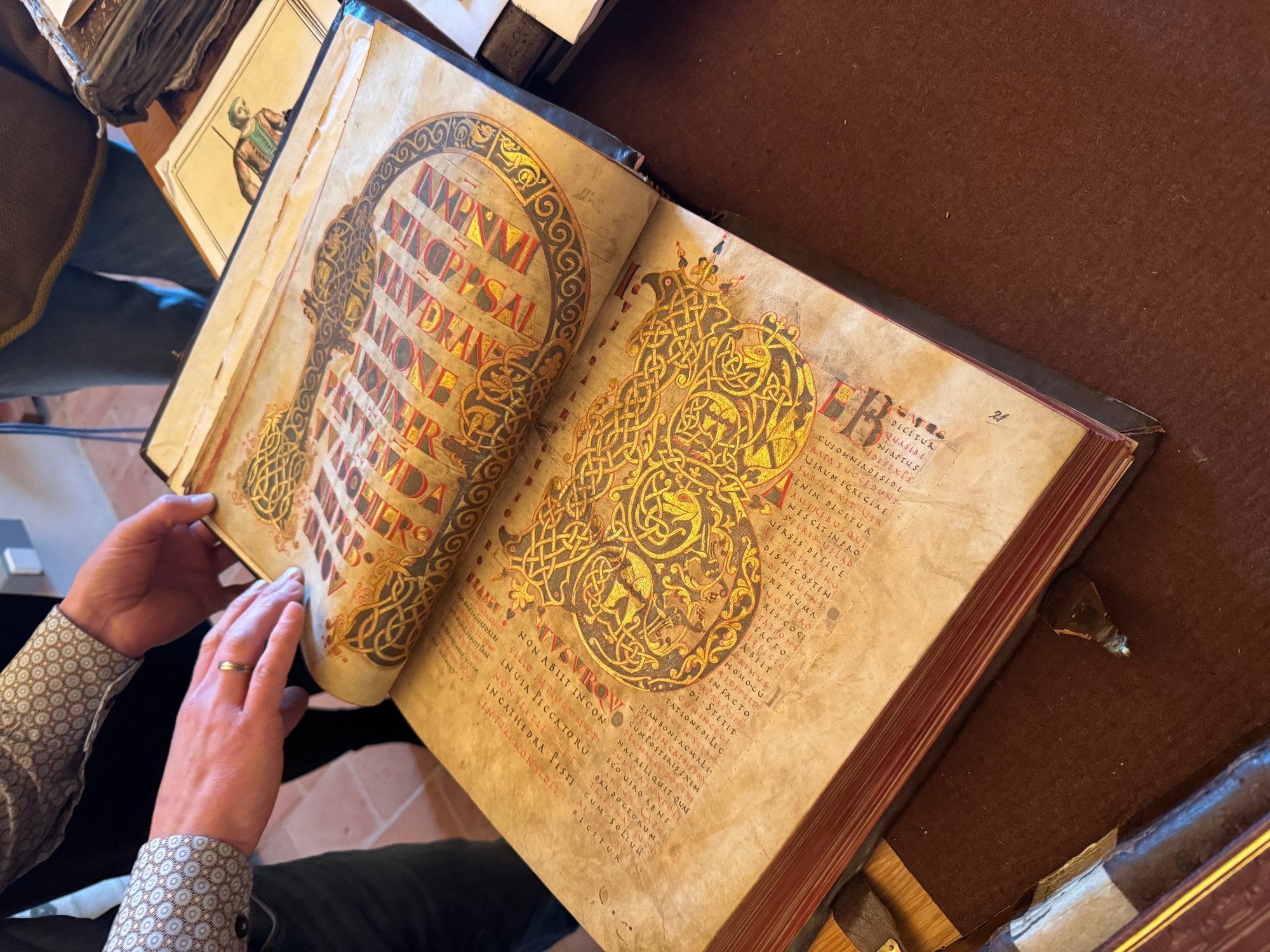 Aufgeschlagenes mittelalterliches Manuskript mit goldverzierten Initialen und kunstvoller Schrift.