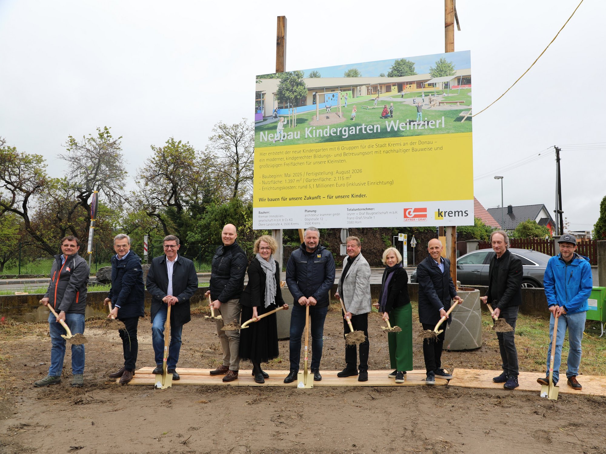 Vertreter aus Politik und Verwaltung mit Spaten vor einer Bautafel mit einem Bild des neuen Kindergartens