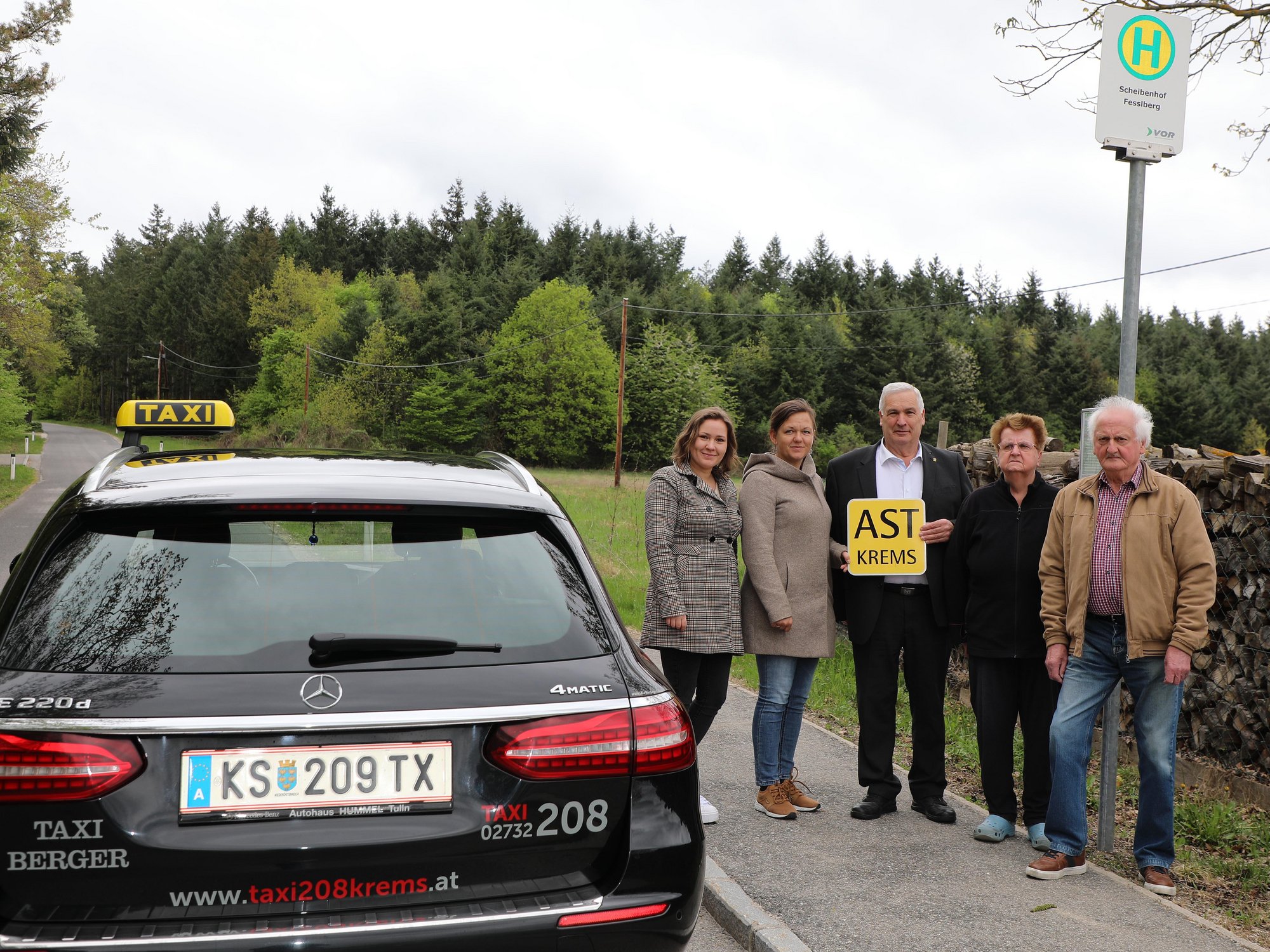 Personengruppe mit Taxi vor der neuen Haltestelle