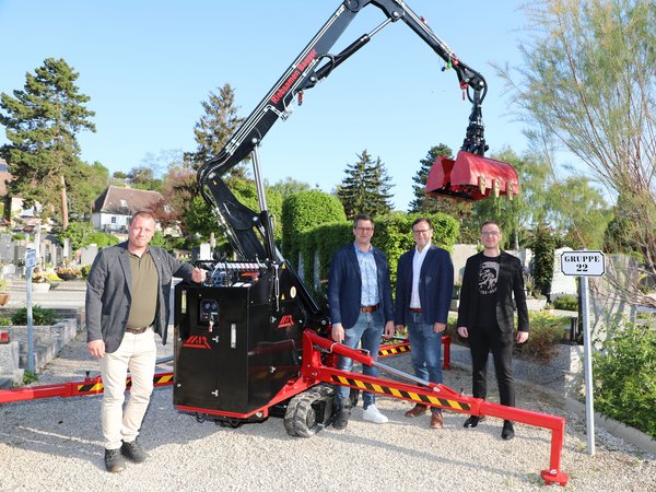 Vier Vertreter der Stadt am Friedhof vor dem neuen Bagger