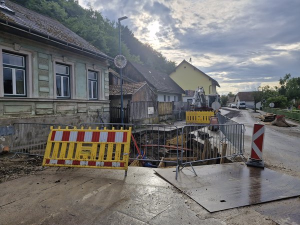 ChatGPT: Straßenbaustelle mit Absperrungen und Bagger in einem Wohngebiet.