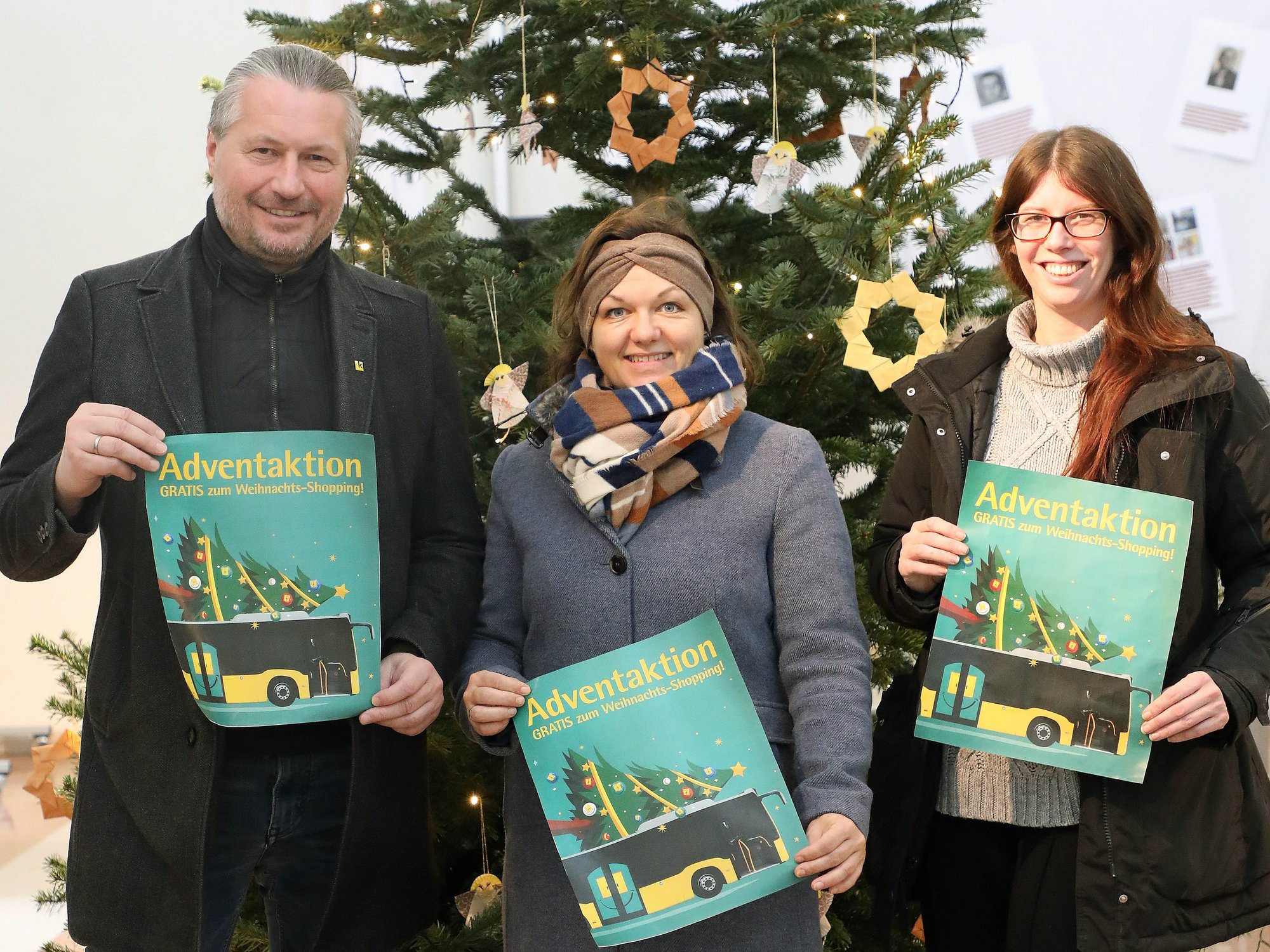 Bürgermeister Peter Molnar, Mobilitätsstadträtin Alexandra Ambrosch und Magistratsmitarbeiterin Jennifer Kittel stehen vor dem Weihnachtsbaum im Kremser Rathaus und halten jeweils ein Werbeplakat für die Adventaktion hoch