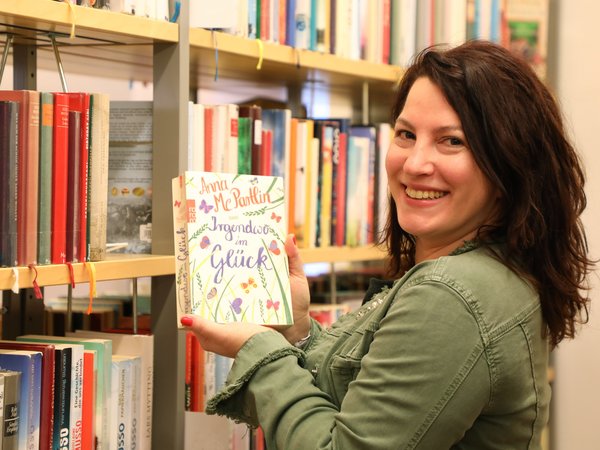 Die neue Stadtbüchereileiterin mit einem Buch in der Hand vor eiinem Bücherregal