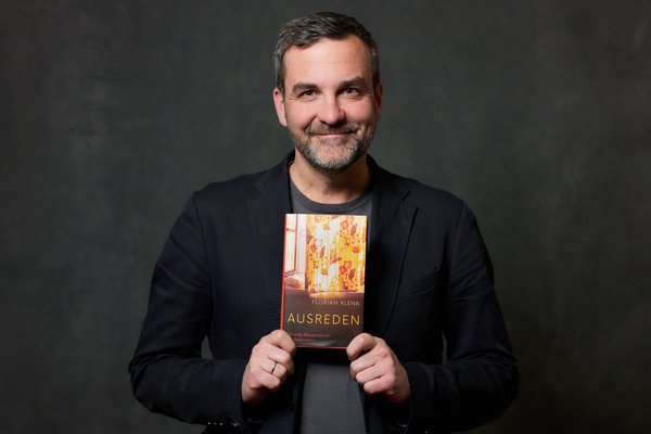 Portrait von Florian Klenk, der lächelnd sein Buch "Ausreden. Elfriede Blauensteiner - Ein Bekenntnis" vor der Brust hält.