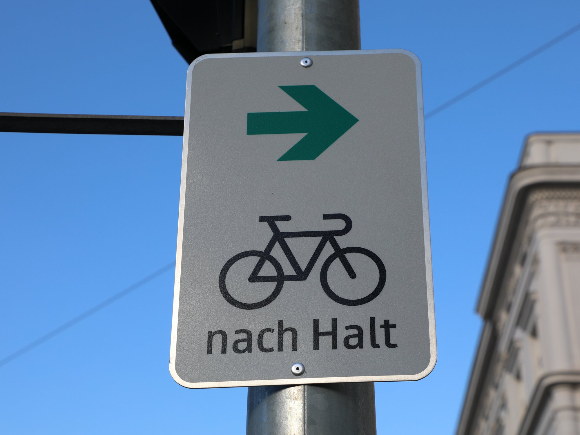 Verkehrsschild mit Fahrrad-Symbol, grünem Pfeil nach rechts und dem Text „nach Halt“.