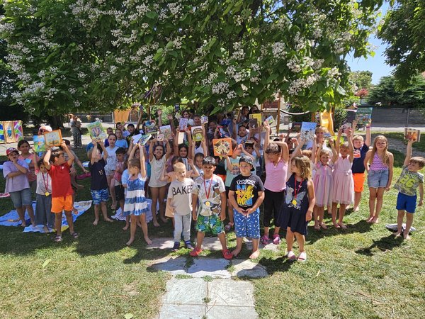 Gruppenfoto von vielen Kindern auf einer Wiese, die Bücher in die Höhe halten