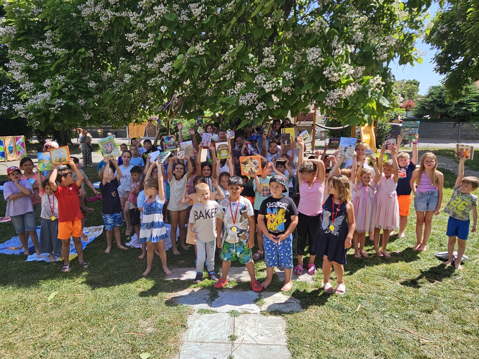 Gruppenfoto von vielen Kindern auf einer Wiese, die Bücher in die Höhe halten