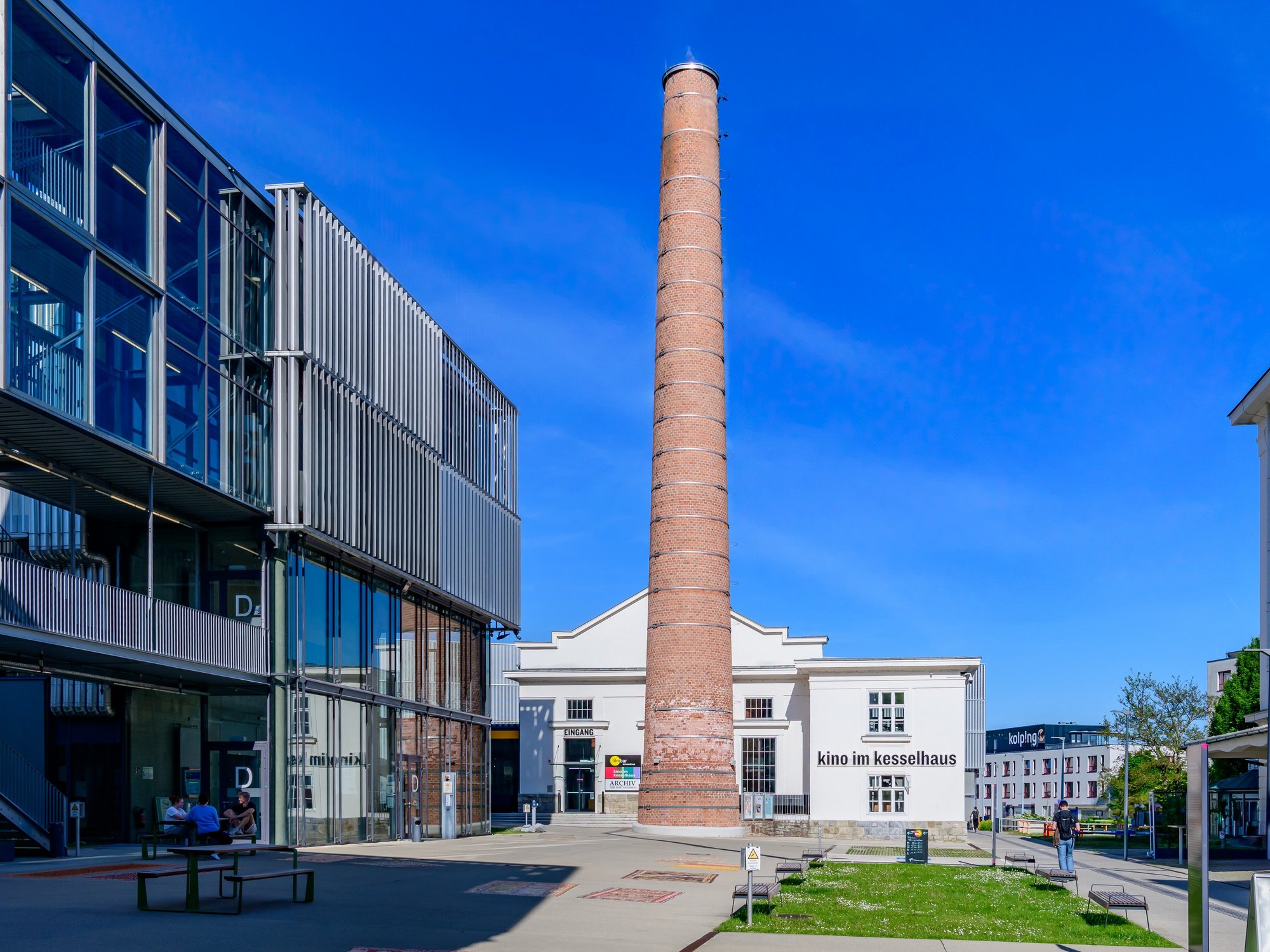 Hof am Unicampus Krems mit modernem Glasbau, Schornstein und dem Kino im Kesselhaus.