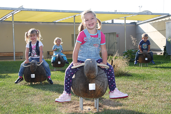 Kinder sitzen auf Schafen aus Holz