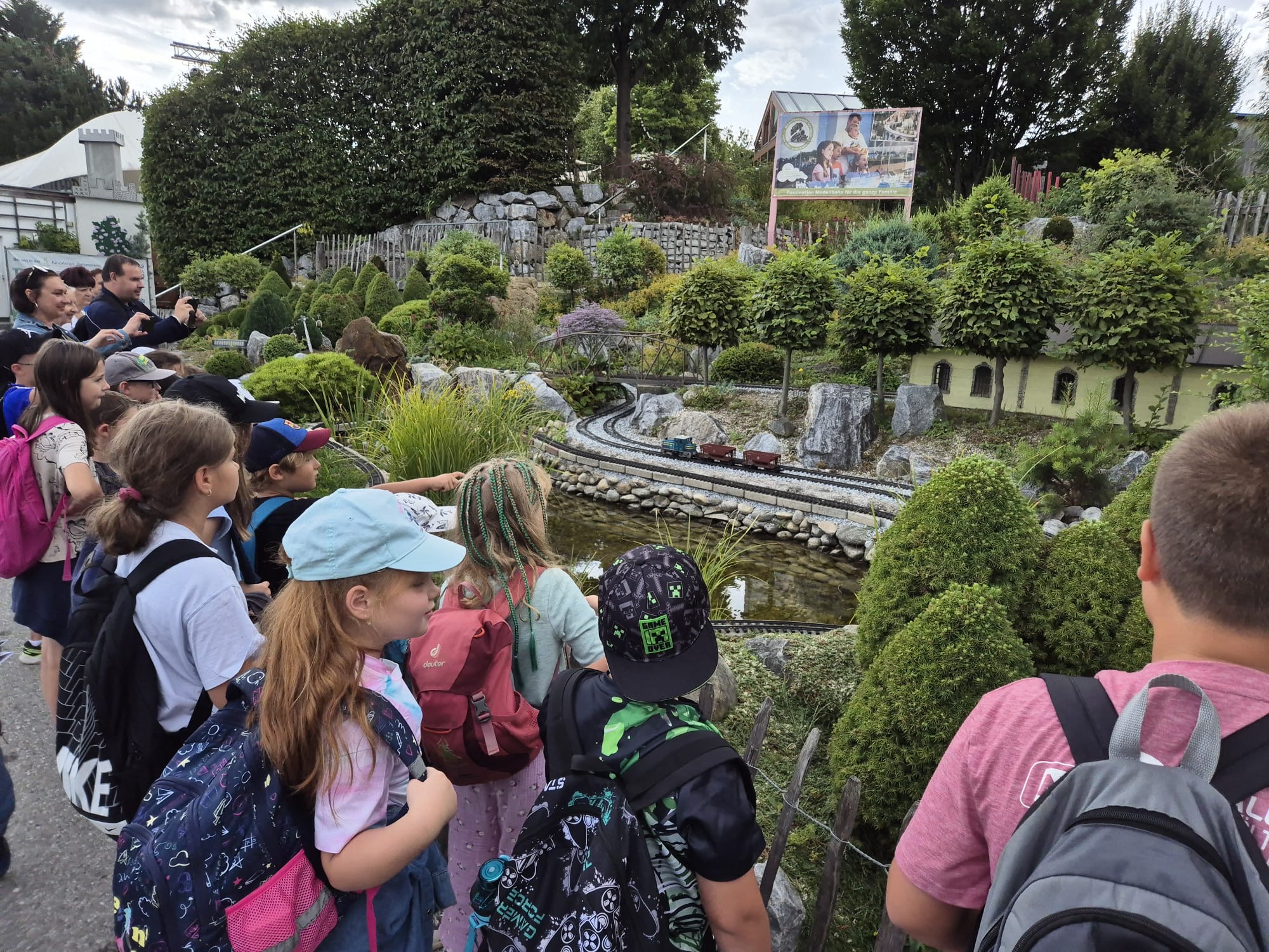Kindergruppe betrachtet eine große Modellbahnanlage im Freien.